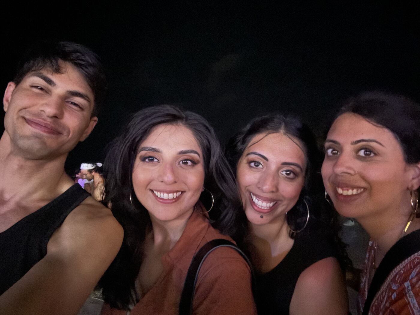 A group of four friends smiling close together in a night-time selfie.